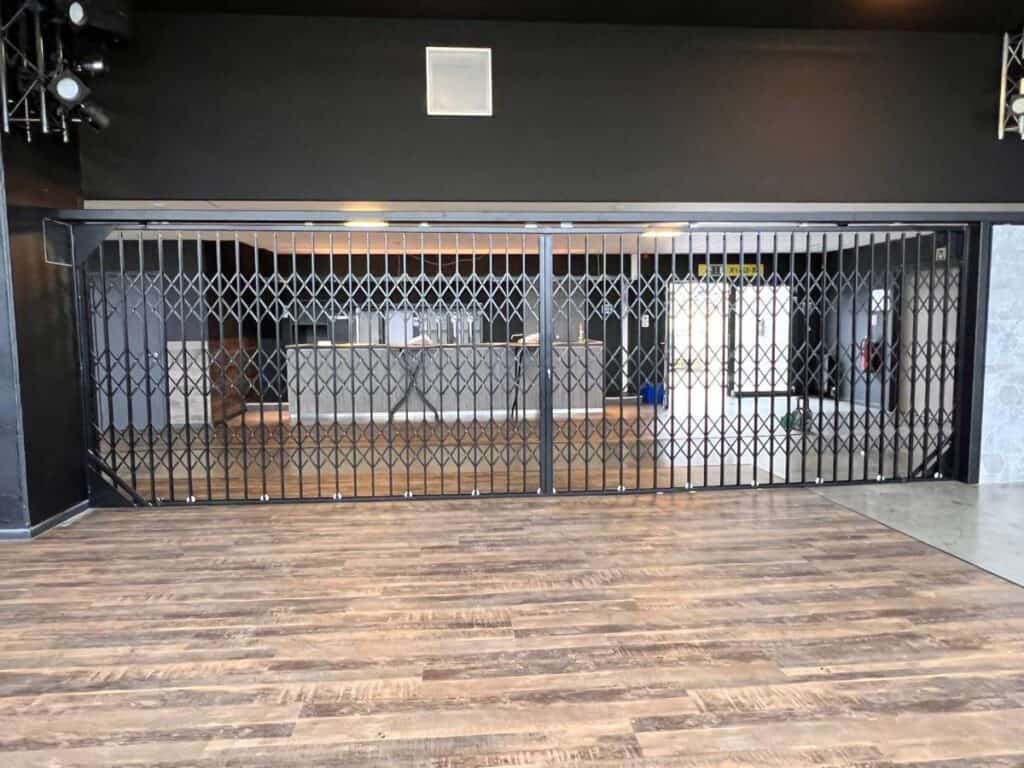 Leeg interieur met houten vloer, zwart metalen hek en ontvangstbalie achter het hek.
