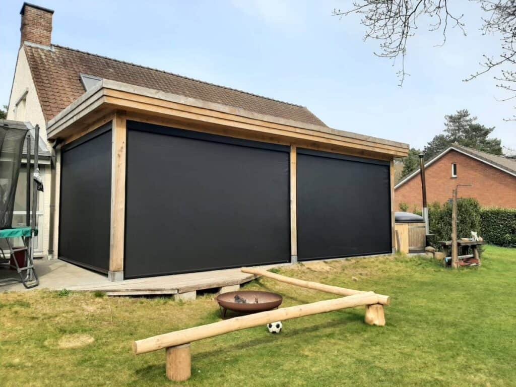 Aangebouwde veranda met zwarte screens, vuurplaats, houten balansbalk en voetbal op grasveld.