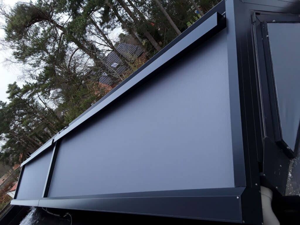Rechthoekig blauw Verandazonwering met zwart metalen frame gemonteerd op gebouw met bomen op achtergrond.