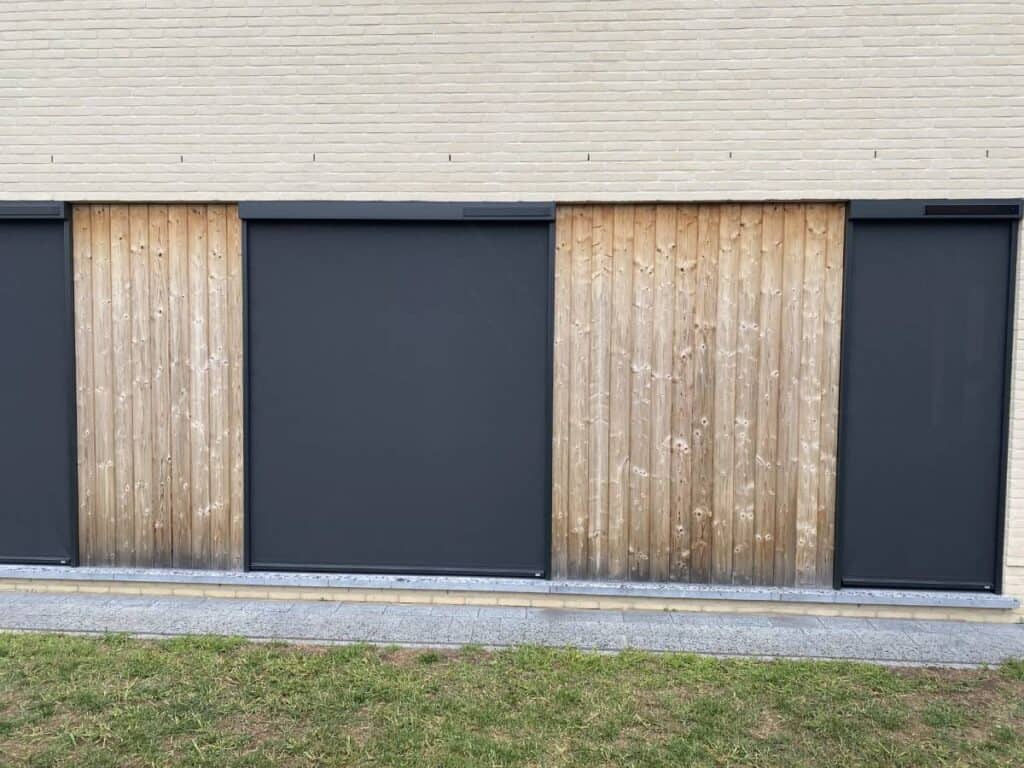 Gevel met lichtgekleurde bakstenen, houten panelen en gesloten zwarte screens, gras en grind.