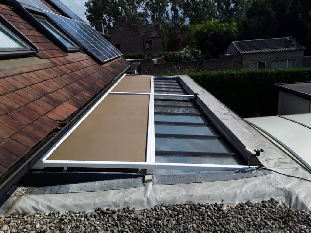 Plat dak met glazen dakraam en Verandazonwering naast schuin pannendak met zonnepanelen en omliggende huizen.