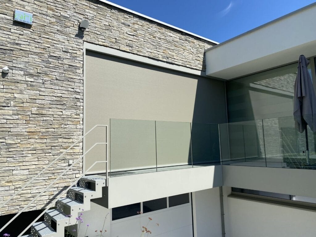 Moderne gevel met lichtkleurige stenen, metalen trap, glazen balustrade en gesloten screens.