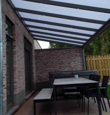 Overdekt terras met buitentafel, zes stoelen, bankje, jacuzzi naast bakstenen huis en houten schutting.